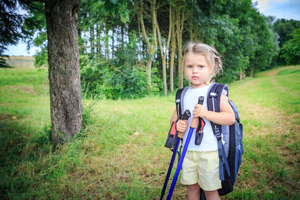 Child on grassy hiking trail carrying her own backpack full of essential hiking gear