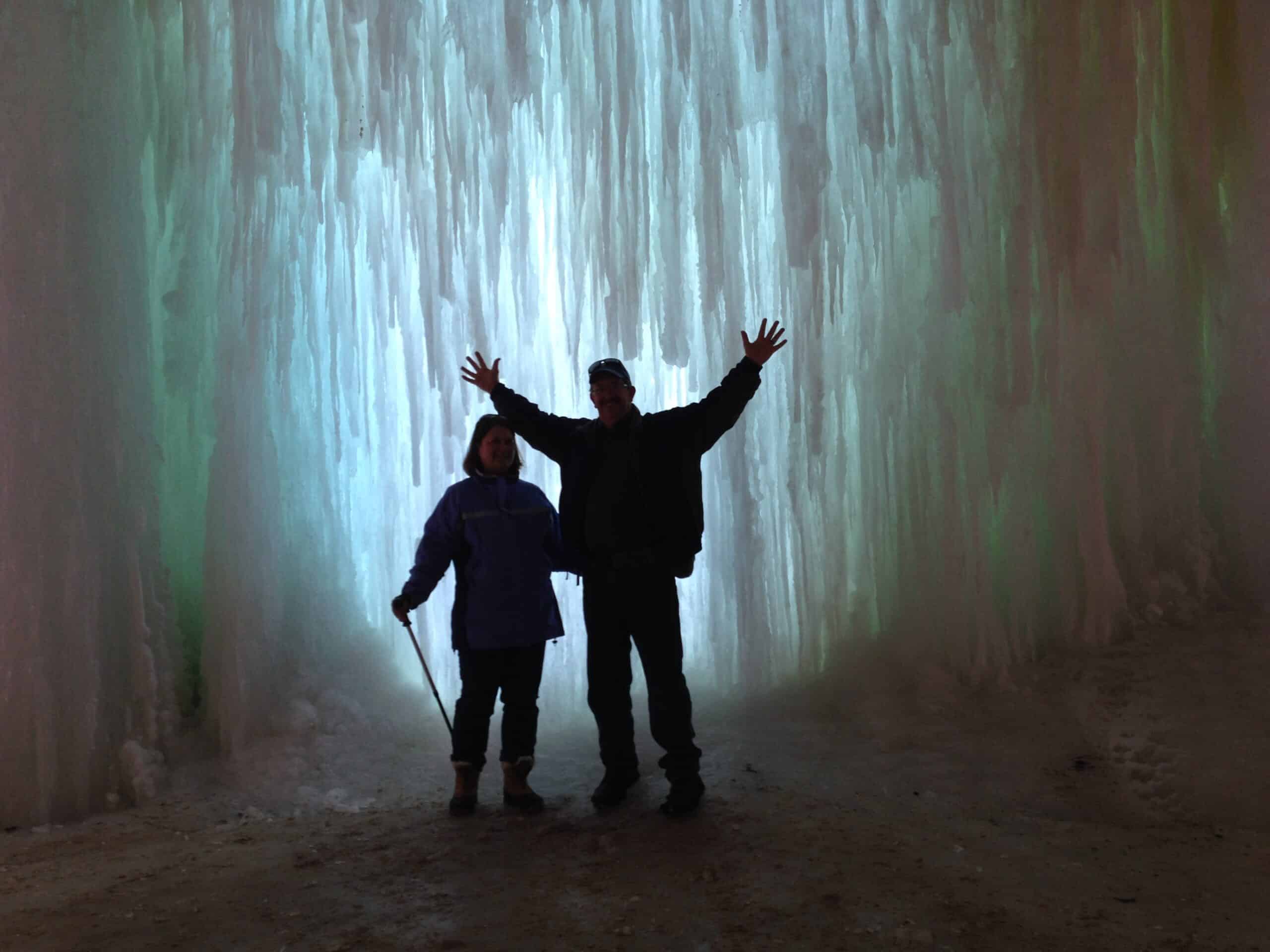 2 people behind a wall of ice with light shining through while winter hiking