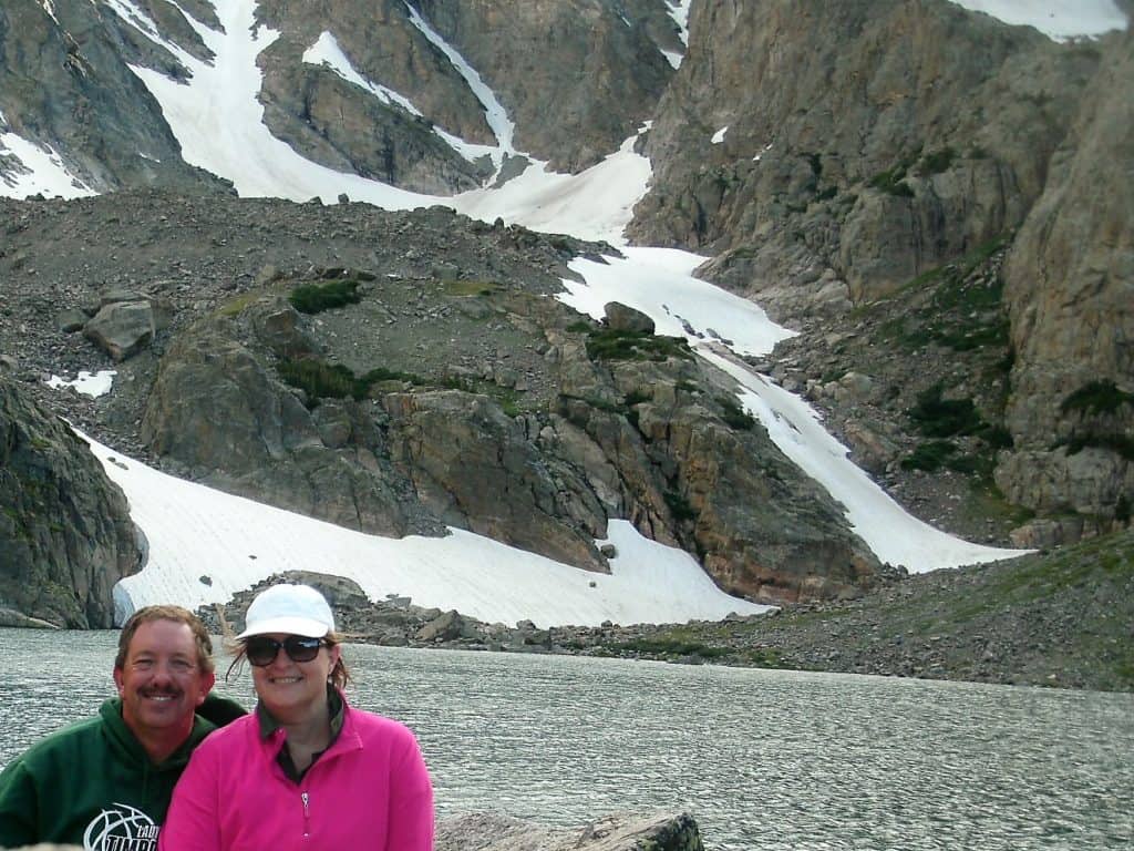 couple sitting next to Sky Pond with lake and mountain wall in background