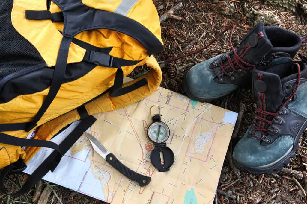 yellow backpack laying on the ground next to map, boots and hiking tools to show what to pack for a day hike