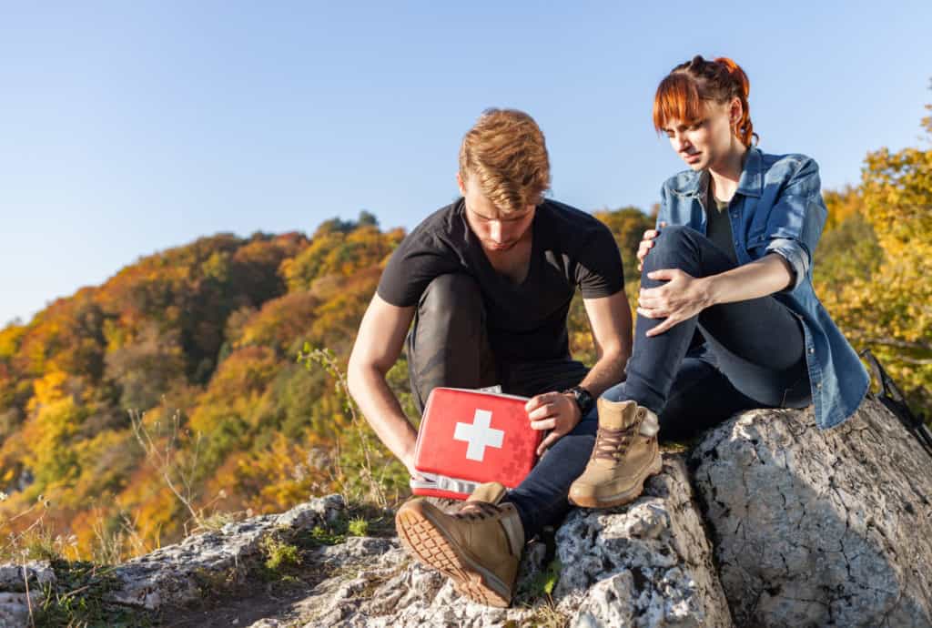 two hikers sitting on rocks looking in first aid kit they packed for their day hike