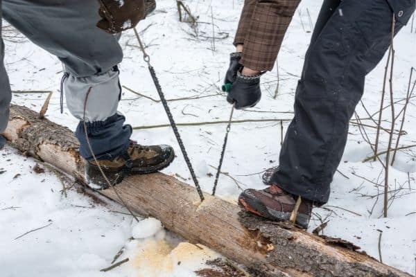 pocket chainsaw being used by 2 men to cut logs for camping