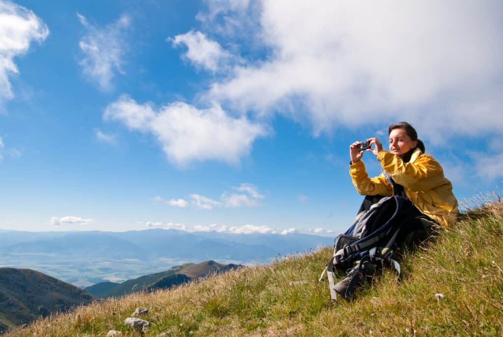 woman sitting on a grassy slope with mountains in the background with her backpack ready for a day hike