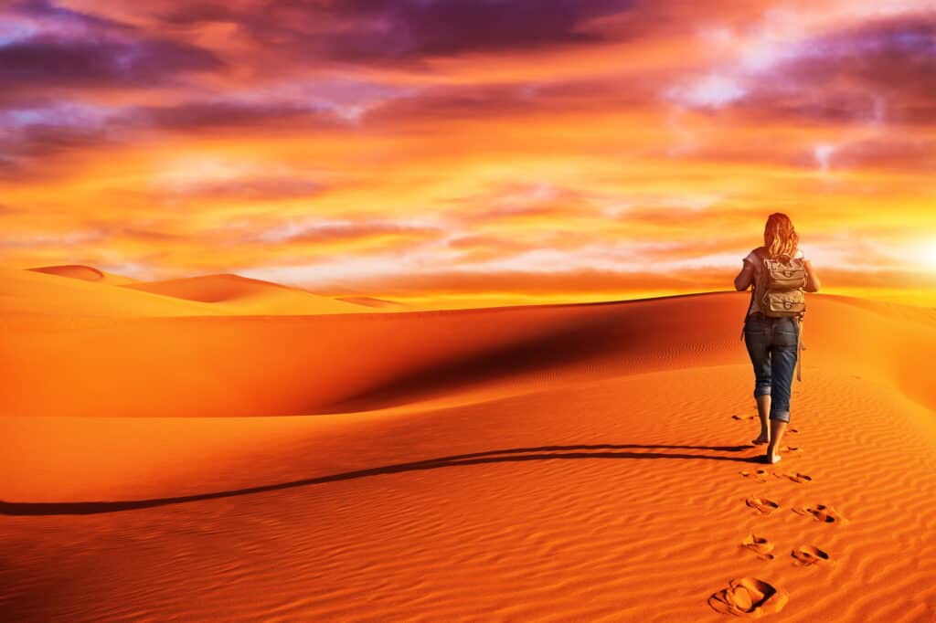 Woman hiking into sun on the dessert, carrying backpack full of essential hiking gear for hot weather