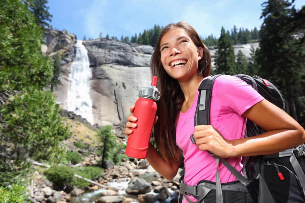 woman hiking with a red water bottle in her hand showing importance of packing water on day hikes