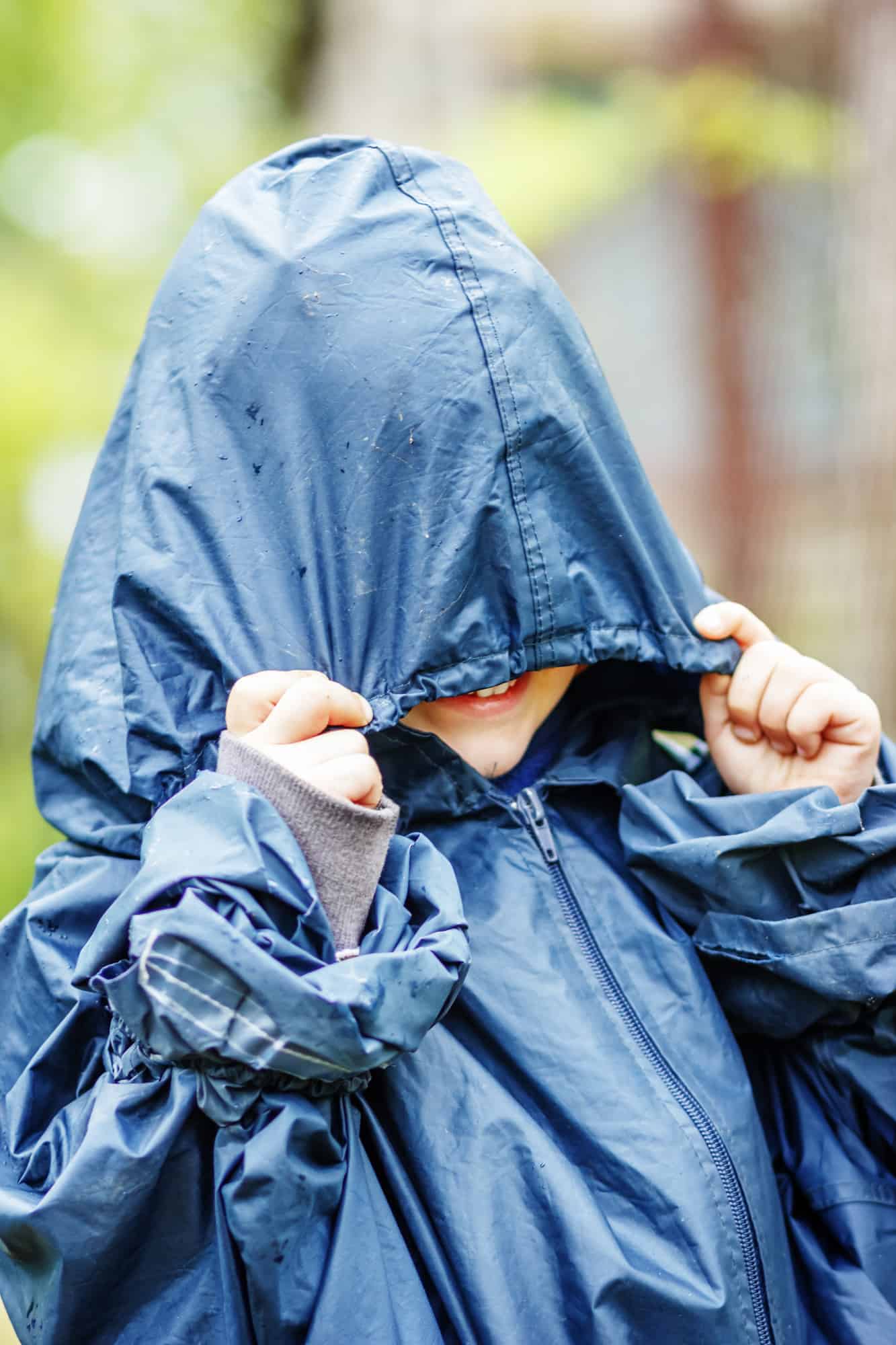 Funny little boy walks in the rain in a raincoat with a hood Walking
