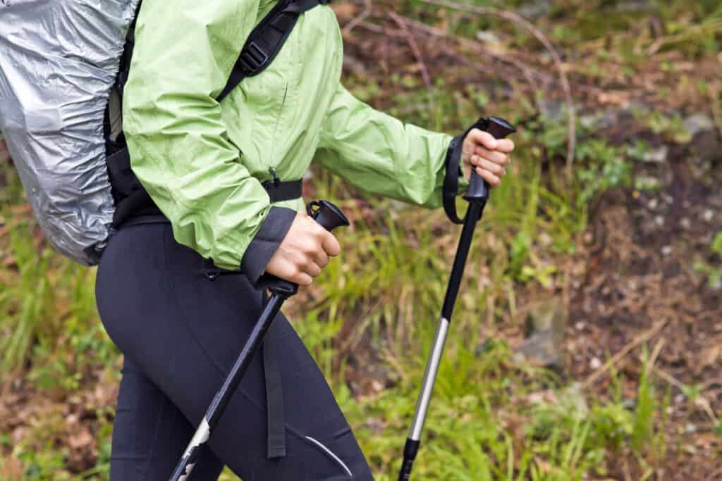 woman walking with hiking poles carrying a backpack that has a rain cover protecting it