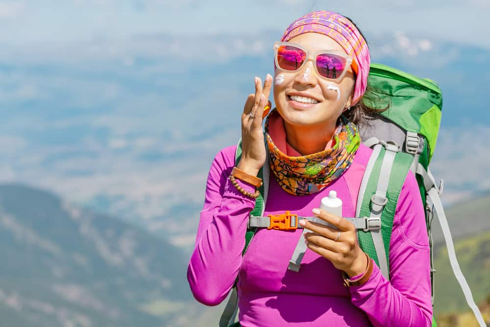 woman hiker applying sunscreen while hiking in the heat