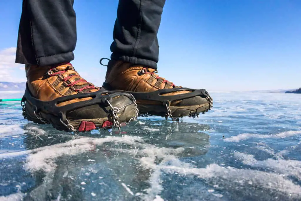 Human legs in hiking boot in microspikes on ice.