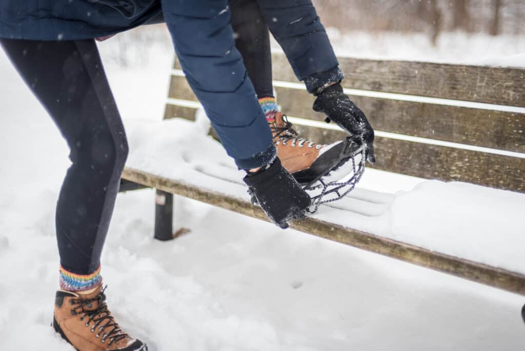 woman getting ready to take hike in snow fixing ice cleat onto boots
