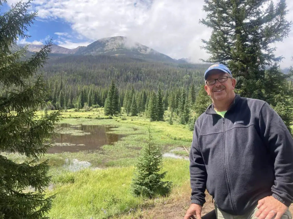 Brad standing in front of beaver pond with evergreen trees in the background