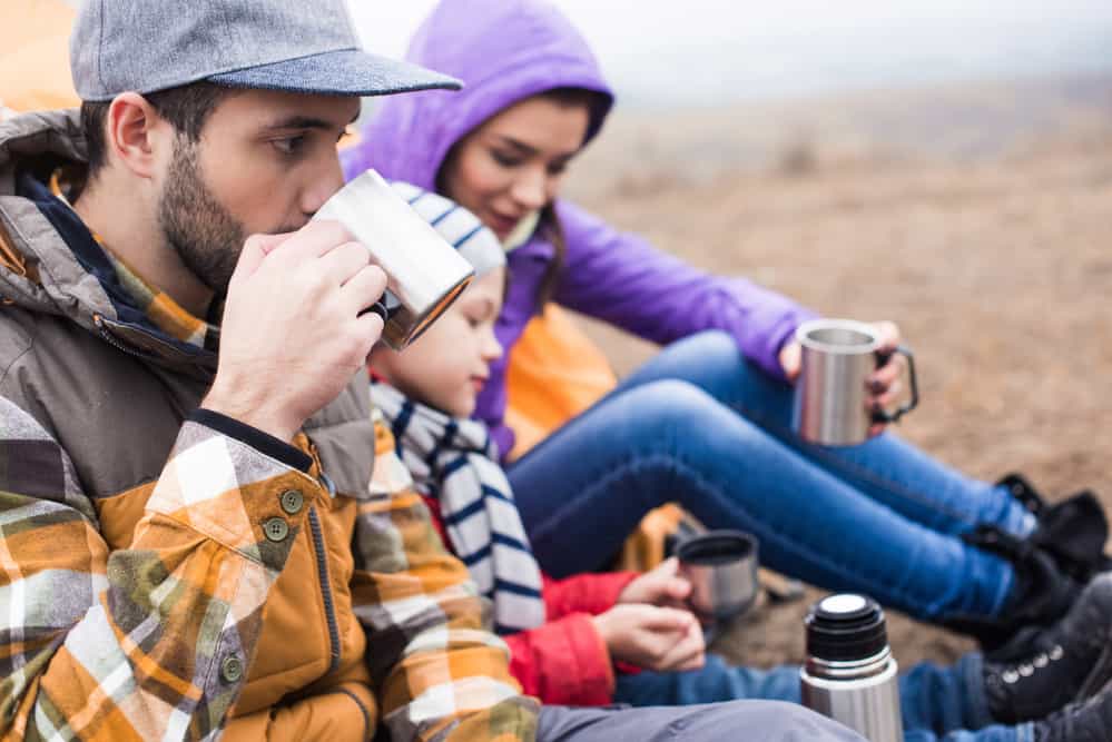 Family resting outdoors after hiking with their lunch of hot soup
