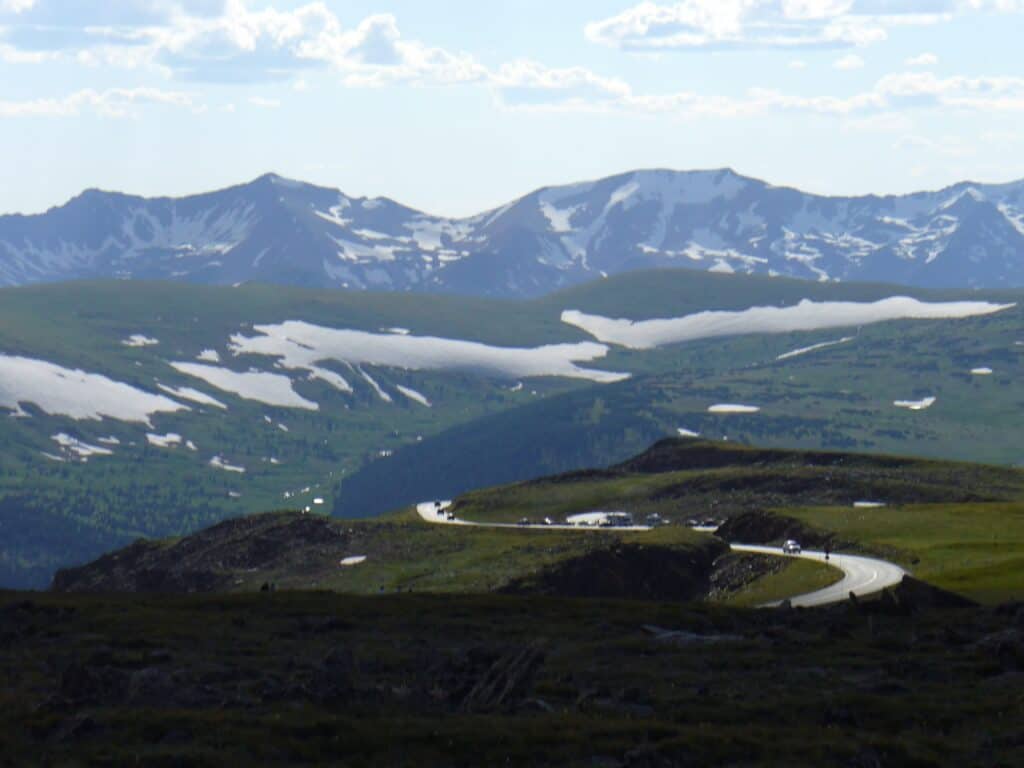 View of Trail Ridge Road S Curve weaving through Rocky Mountain National park with snow and mountains in distance. Include in your RMNP 1 day itinerary.