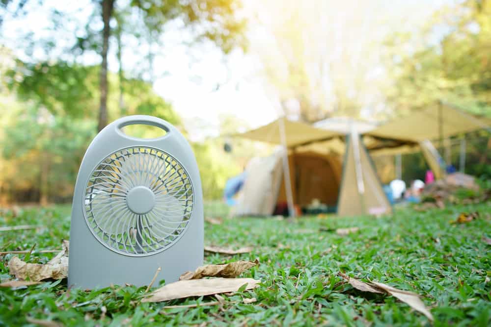 mini camping fan on green grass with tent in background to help keep insects away from campsite