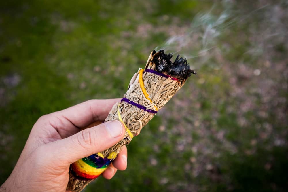 Sage Smudge Stick burning, held by a hand against green grass to get keep away mosquitoes