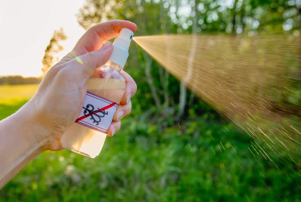 spray bottle against grassy background spraying essential oil as a way to repel mosquitoes while hiking