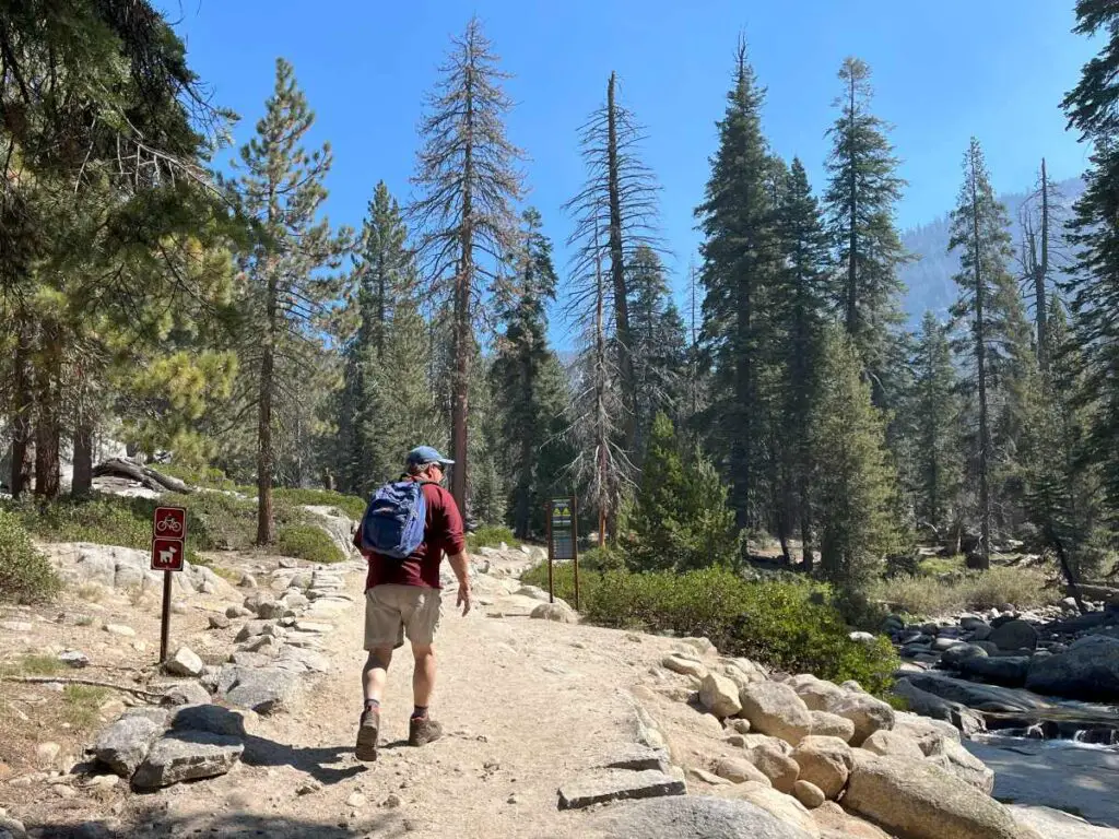 Man hiking on gravel trail with stream on right