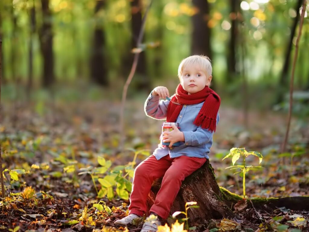 small child sitting on tree stump eating a snack