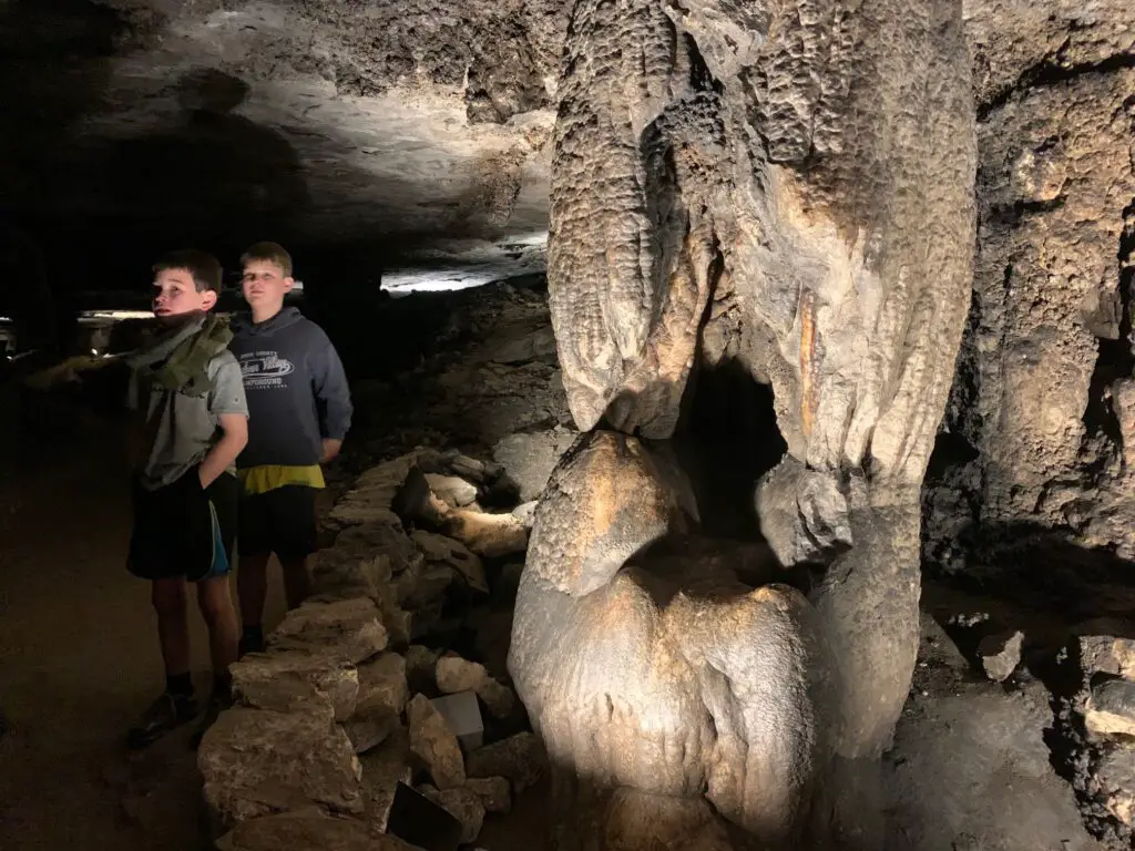 2 boys standing next to cave structure that looks like a throne. From the Gothic Avenue Tour at Mammoth Cave National Park