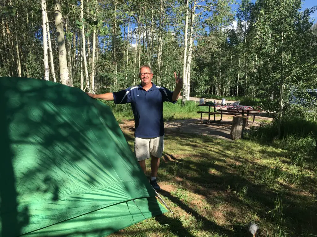 green tent with man wearing blue shirt in a forest