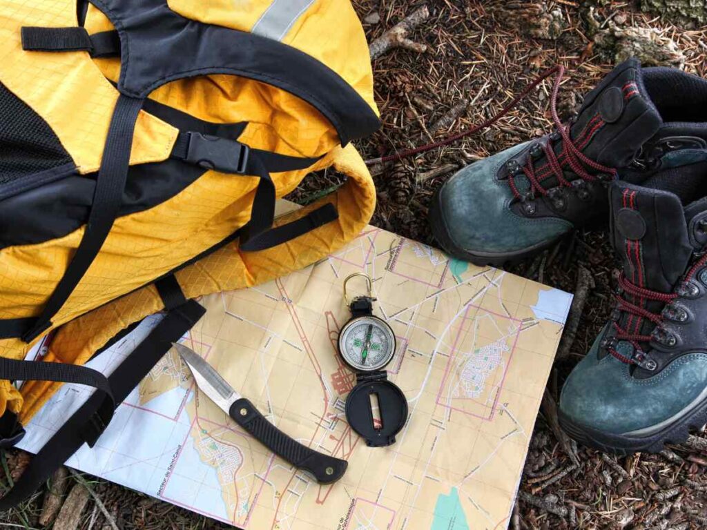 Yellow backpack next to map, compass and hiking boots