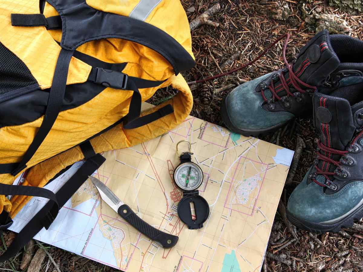 Yellow backpack next to map, compass and hiking boots