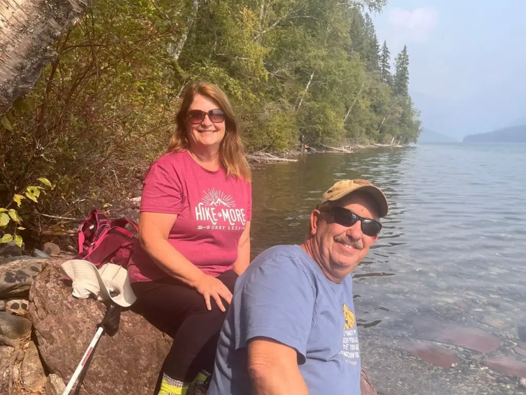 Man and woman sitting on rocks near lake with hiking gear