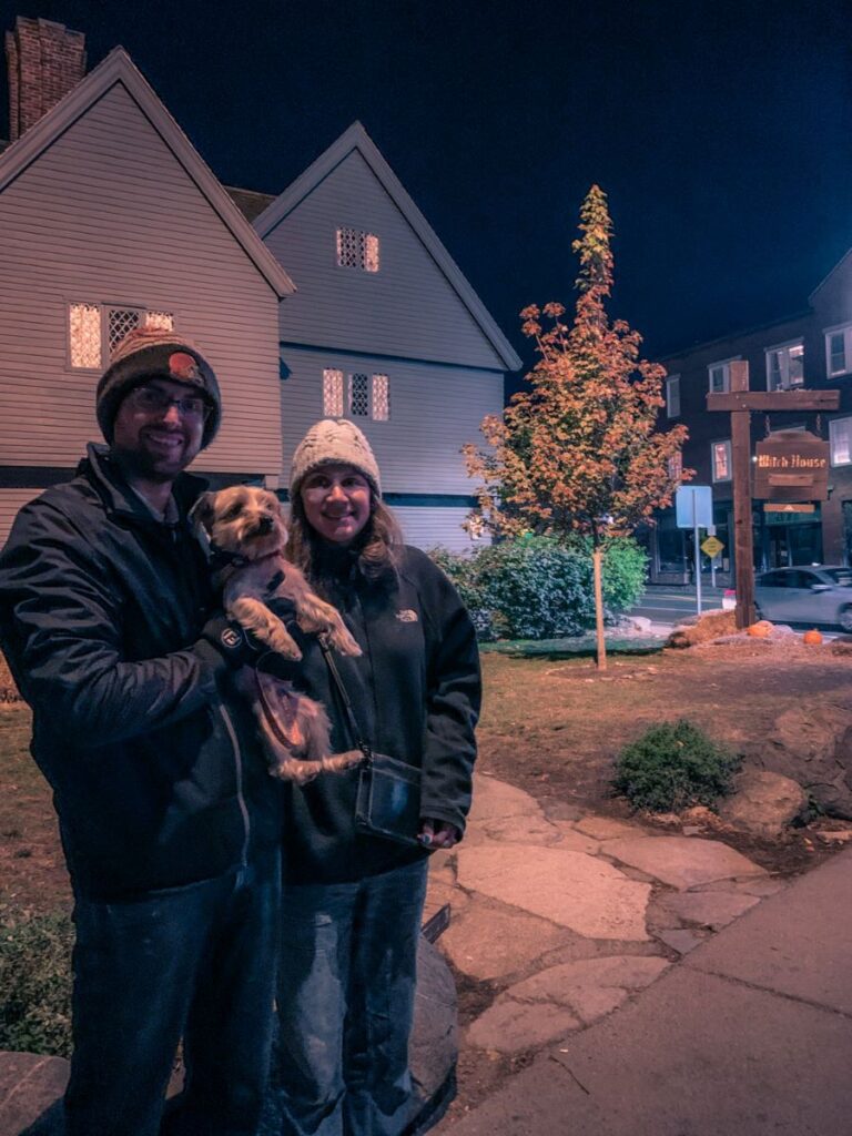 Man and Woman Holding small dog in front of Witch House