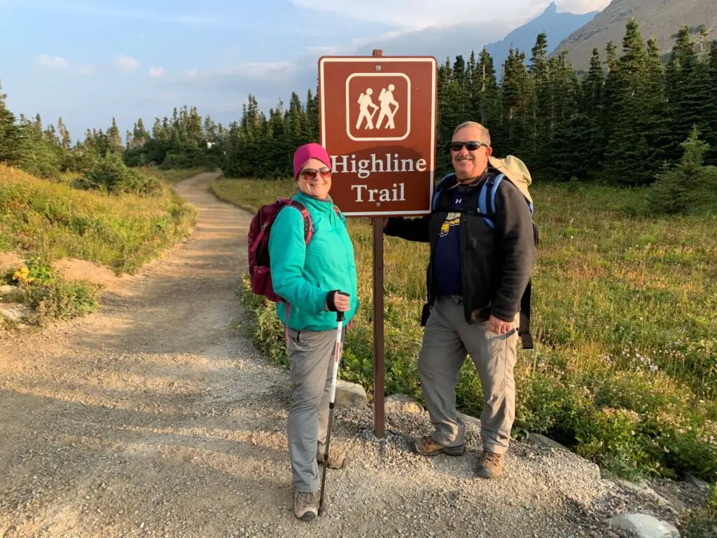 Man and woman standing next to sign for Highline Trail, trail starts in the background