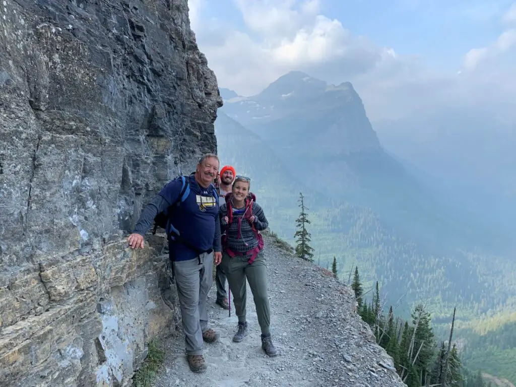 3 hikers standing on narrow trail with steep cliff drop off on the Highline Trail in Glacier National Park