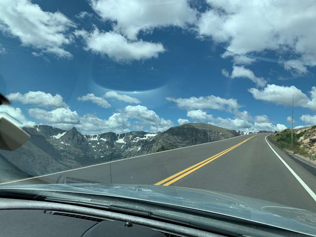 View of highway out the front window of silver car. Rocky Mountains to the side.