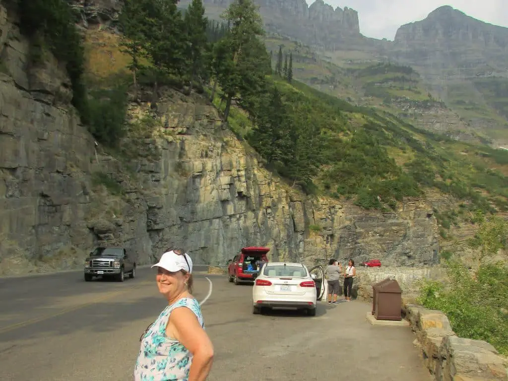 Ladona standing on Going to the Sun Road in a pull off. white, red and black car in background.