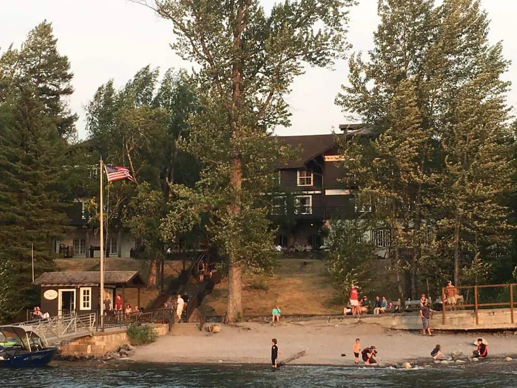 View of the back of Lake McDonald Lodge, showing beach area with people on the beach.