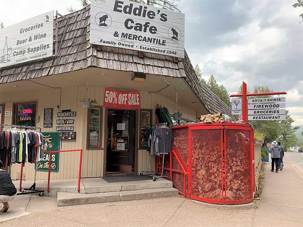 Eddies Cafe store front in Apgar Village, advertising camping supplies and lunch options. Stack of firewood in front. Just off Going to the Sun Road