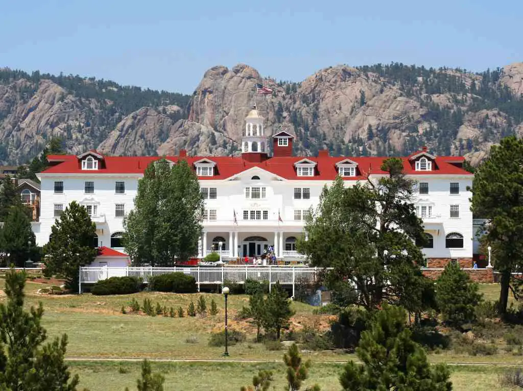 White Front of Stanley Hotel against mountains in background -  which is unique lodging in Rocky Mountain National Park.