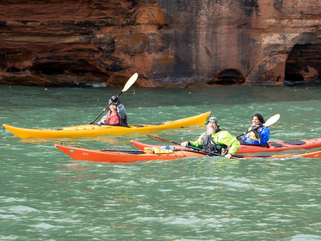 3 people kayaking against rock wall background