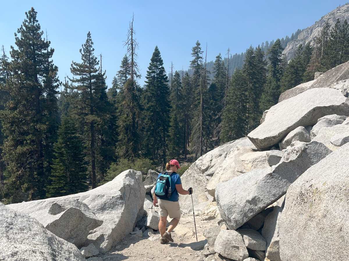 woman with blue backpack hiking between boulders in sequoia national park