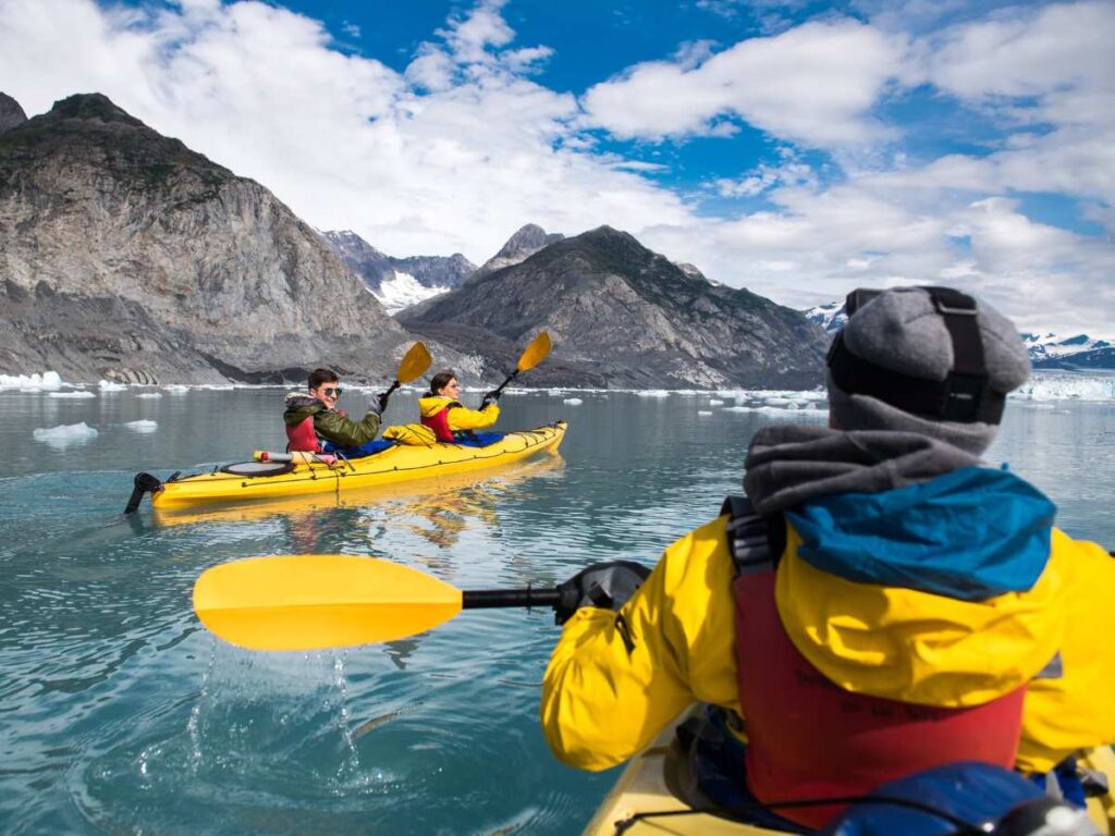 2 yellow kayaks with 3 people on the water at the base of bear glacier in Kenia Fjords