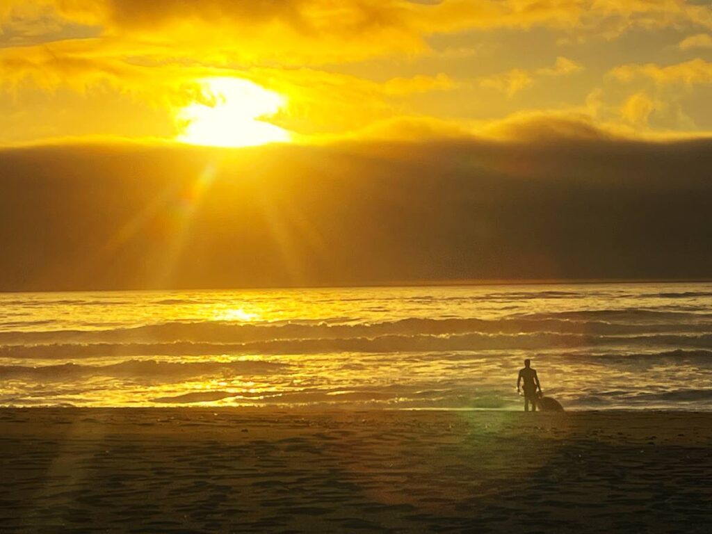 sunset over the ocean with beach in front. man with kayak standing on beach