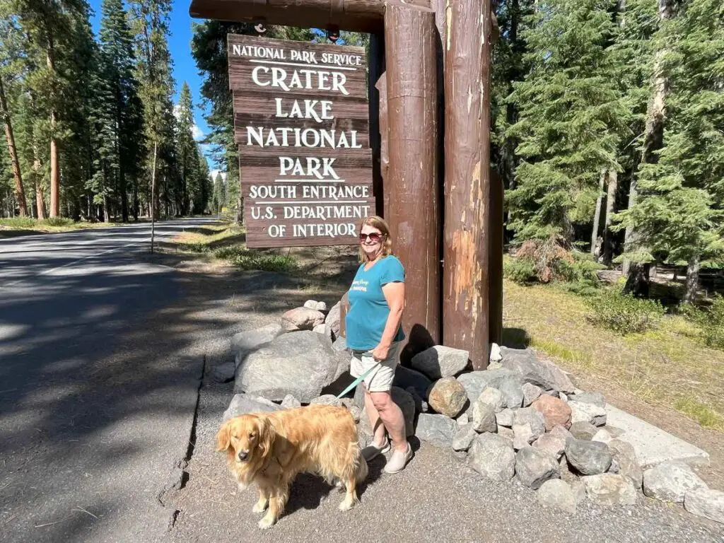 Woman with dog standing next to Crater Lake Welcome Sign