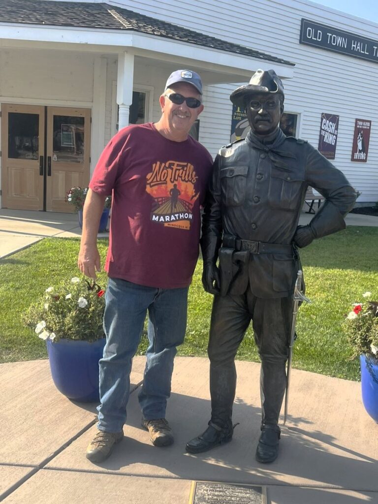 Man posing with bronze statue of Theodore Roosevelt